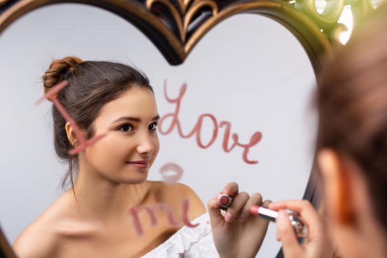 A woman uses lipstick to write "I love you" to herself in the mirror.