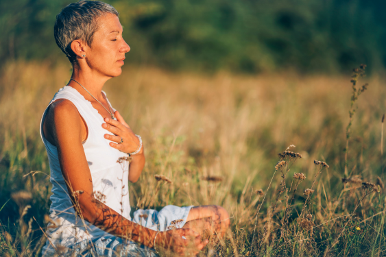 The woman is enjoying the spiritual growth brought by Self-Love after meditating on the grassland.