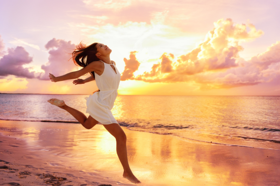 Woman (know Love yourself) in white dress jumping happily on the beach at sunset