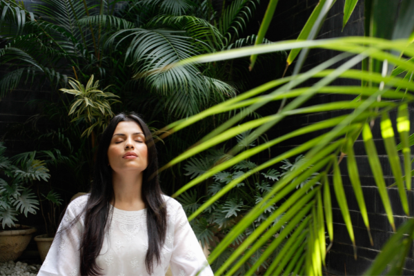 A girl meditates surrounded by green plants