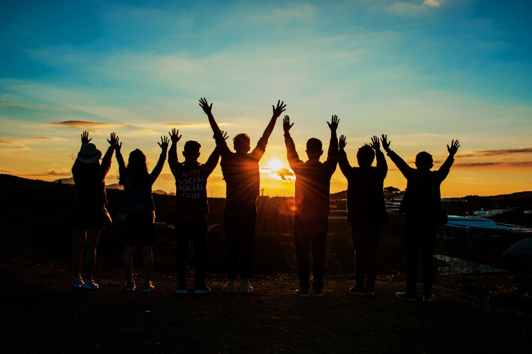 A group of friends stood high with their hands in front of the sunset and cheered